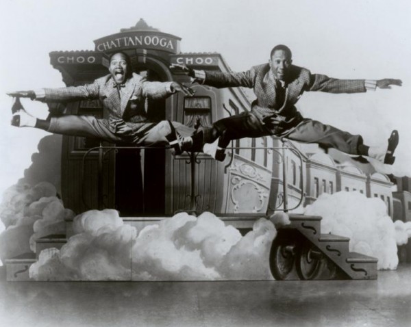 The Nicholas Brothers in side split leaps in front of a stage set featuring a railroad caboose labeled "Chatanooga Choo Choo," 1941. 